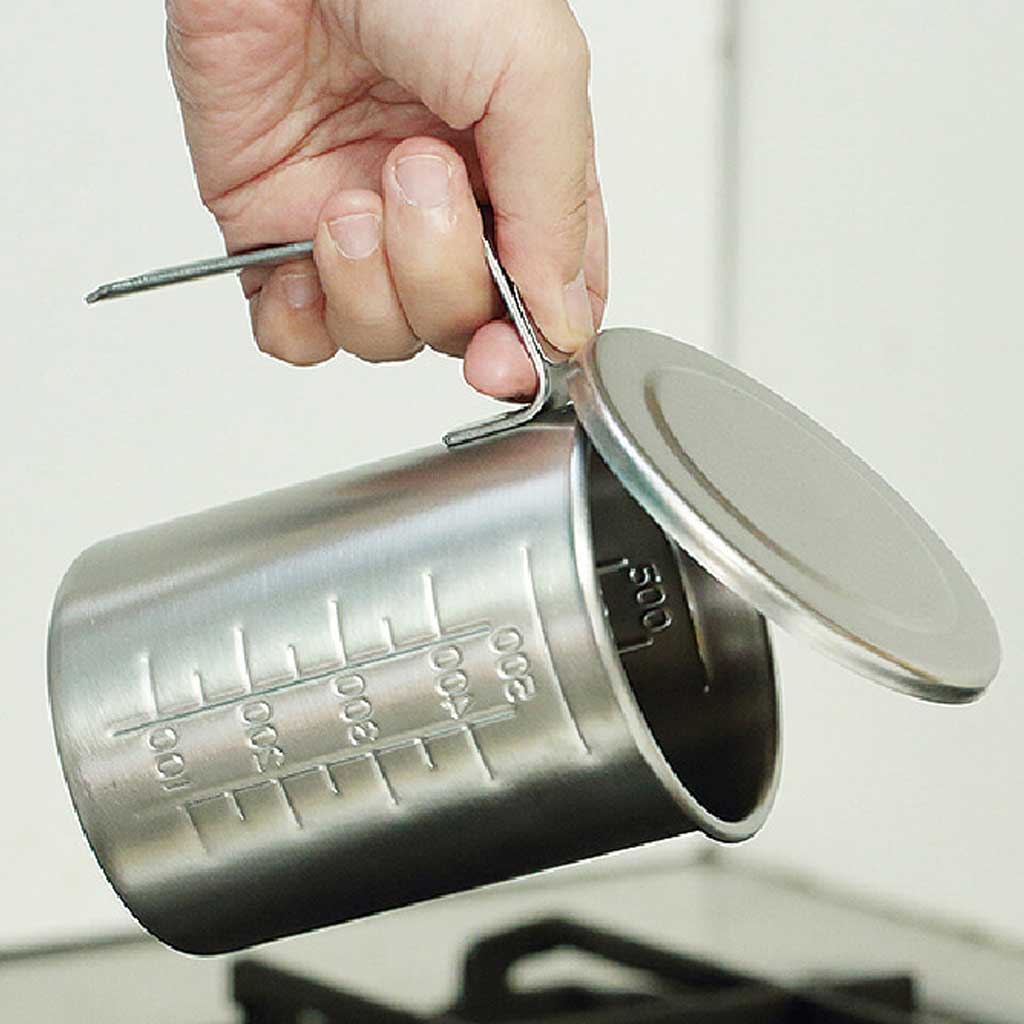Metal measuring cup with handle and measurement markings, held by a hand.