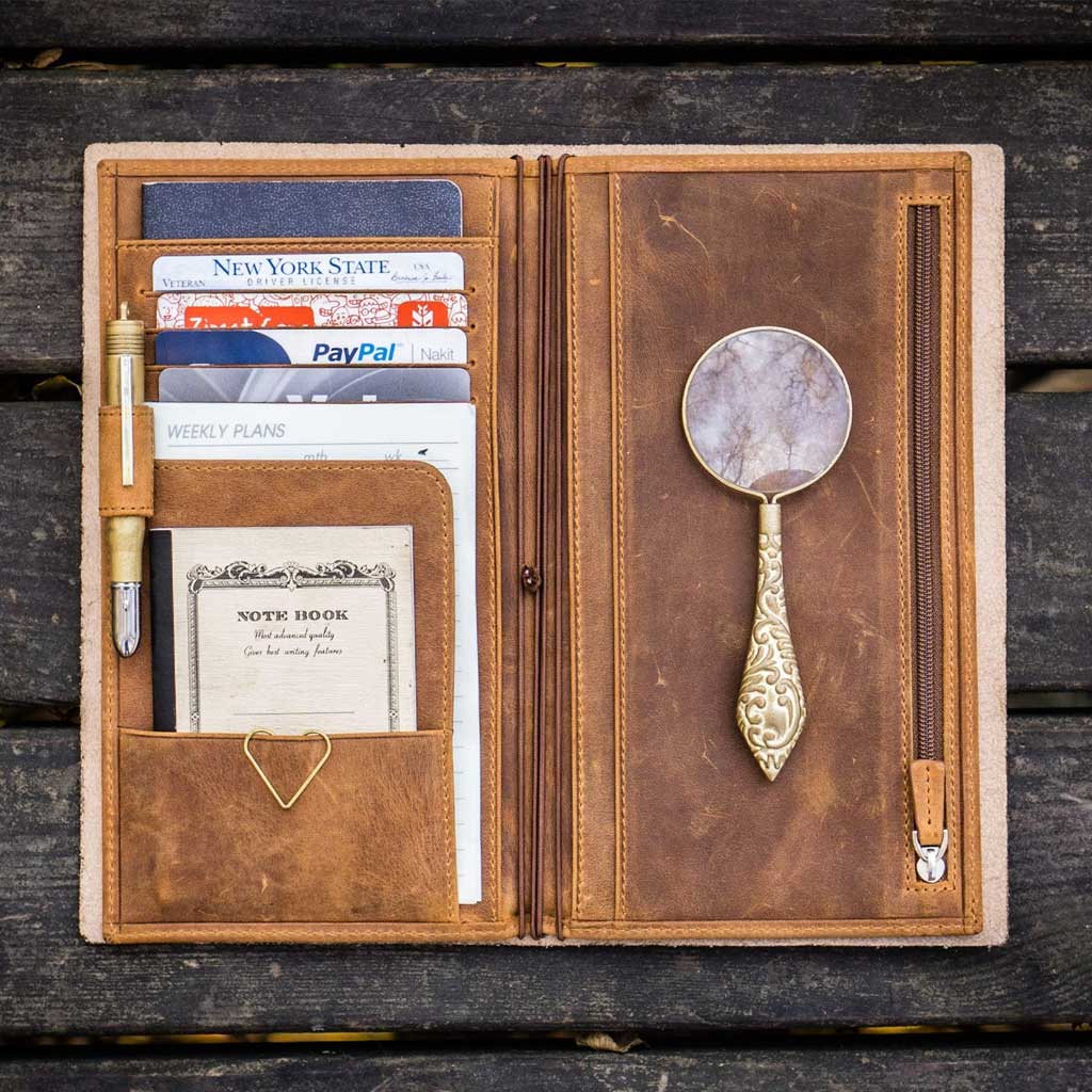 Brown leather Traveler's Notebook wallet insert with clips and papers on wooden surface