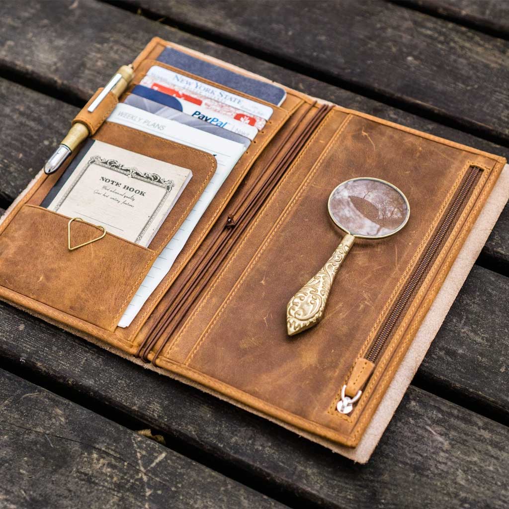 Brown leather Traveler's Notebook wallet insert with clips and papers on wooden surface