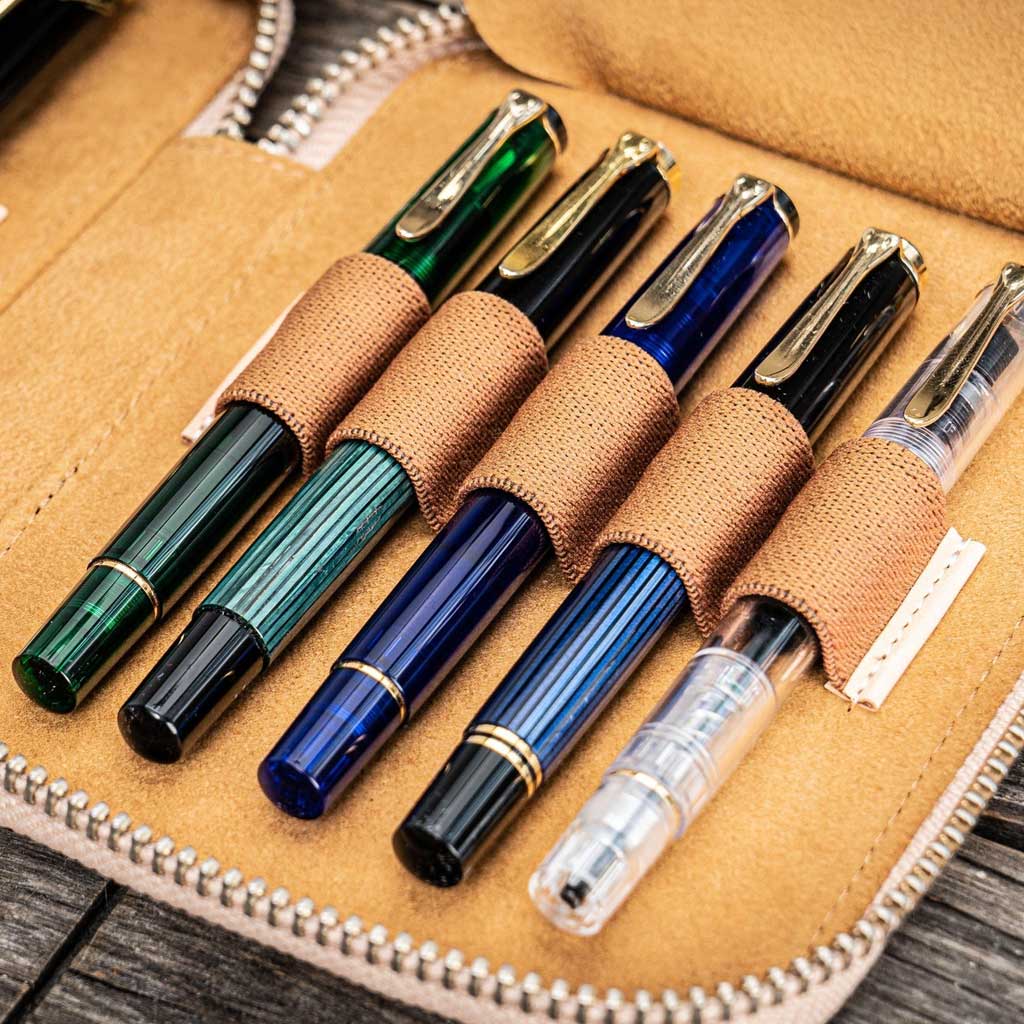 Natural undyed leather pen case with zipper and five pens on a wooden surface