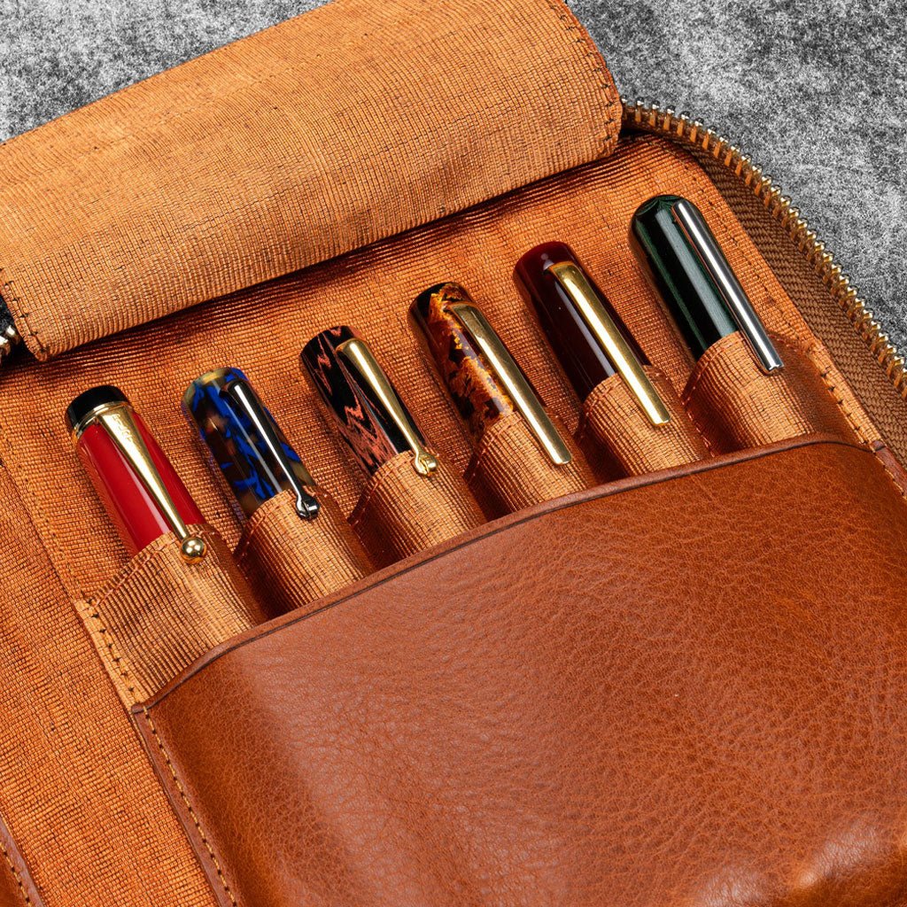 Brown leather zip pen case with writing tools against dark background