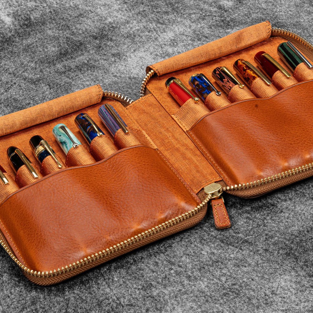 Brown leather zip pen case with writing tools against dark background