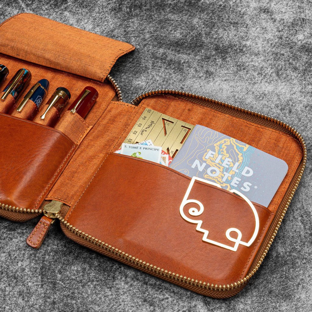 Brown leather zip pen case with writing tools and stationery supplies against dark background