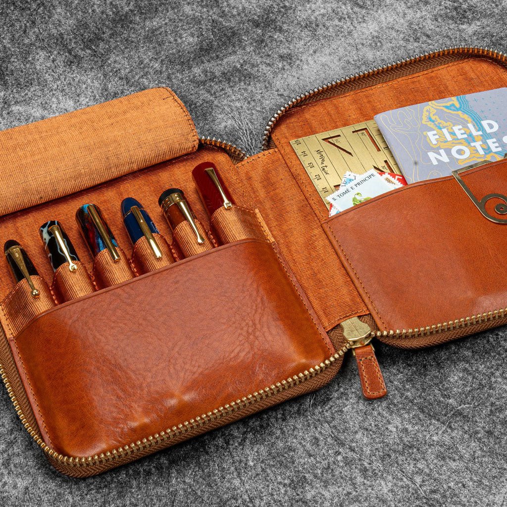 Brown leather zip pen case with writing tools and stationery supplies against dark background