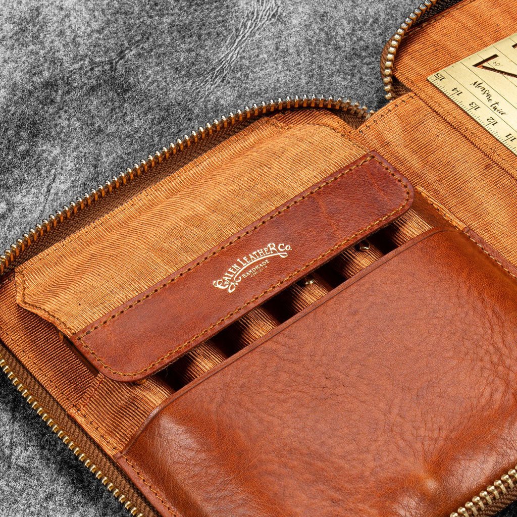 Brown leather zip pen case with writing tools and stationery supplies against dark background