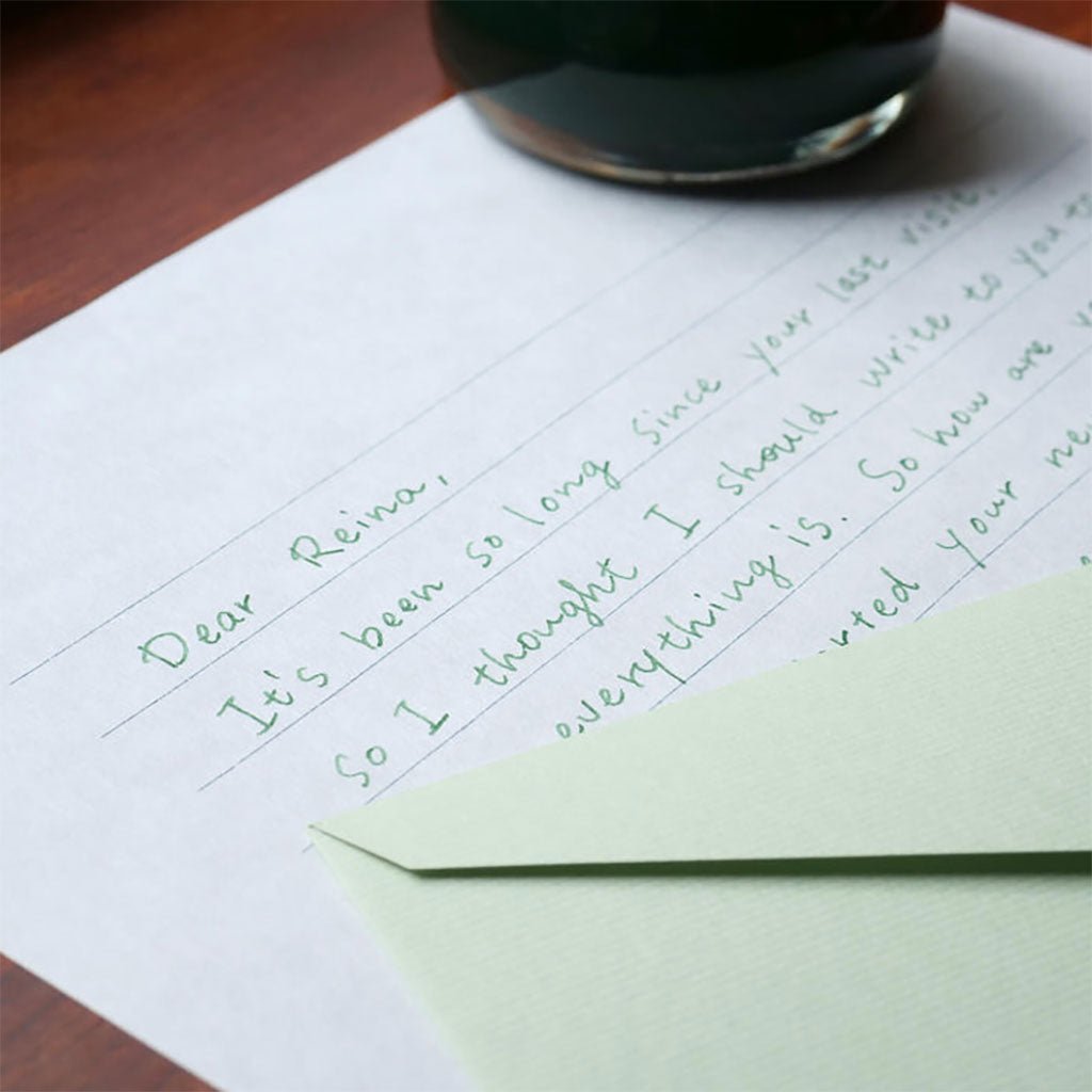 Handwritten letter on lined paper with a green envelope on a wooden surface.