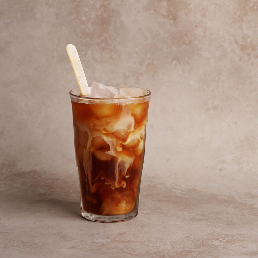 Glass of iced coffee with a long drink spoon on a beige background