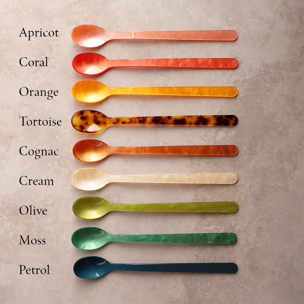 Set of colorful spoons arranged in a row on a textured surface with color names listed.