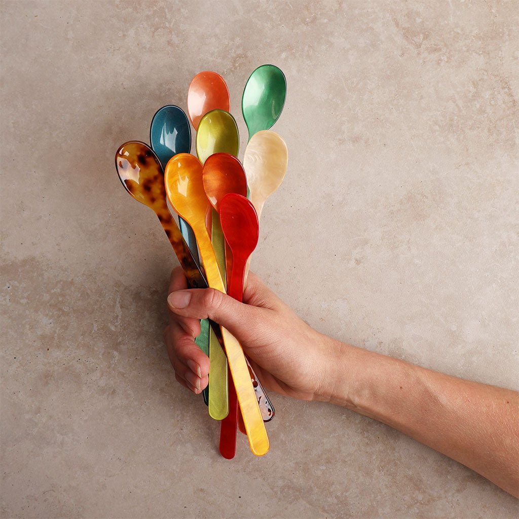 Hand holding a set of colorful acrylic spoons against a beige background
