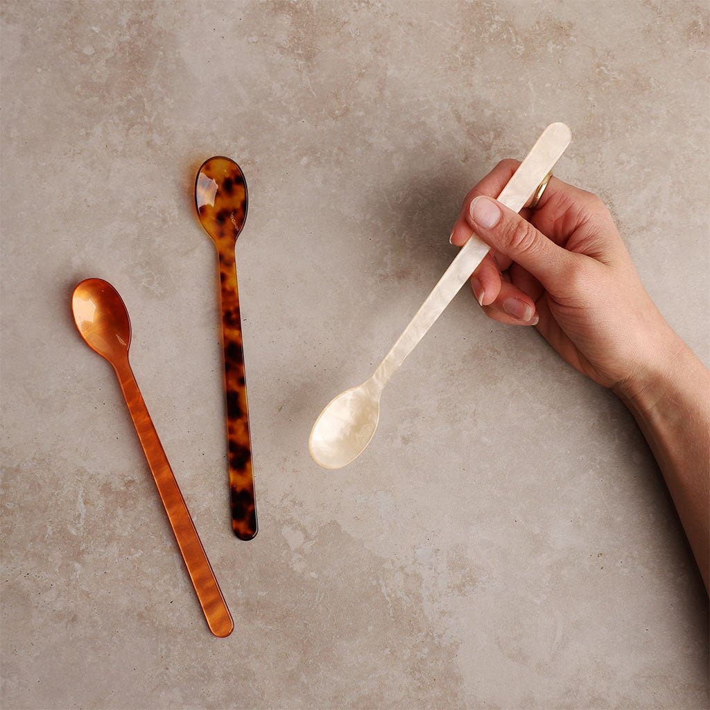 Three spoons on a textured surface with a hand holding one of them.