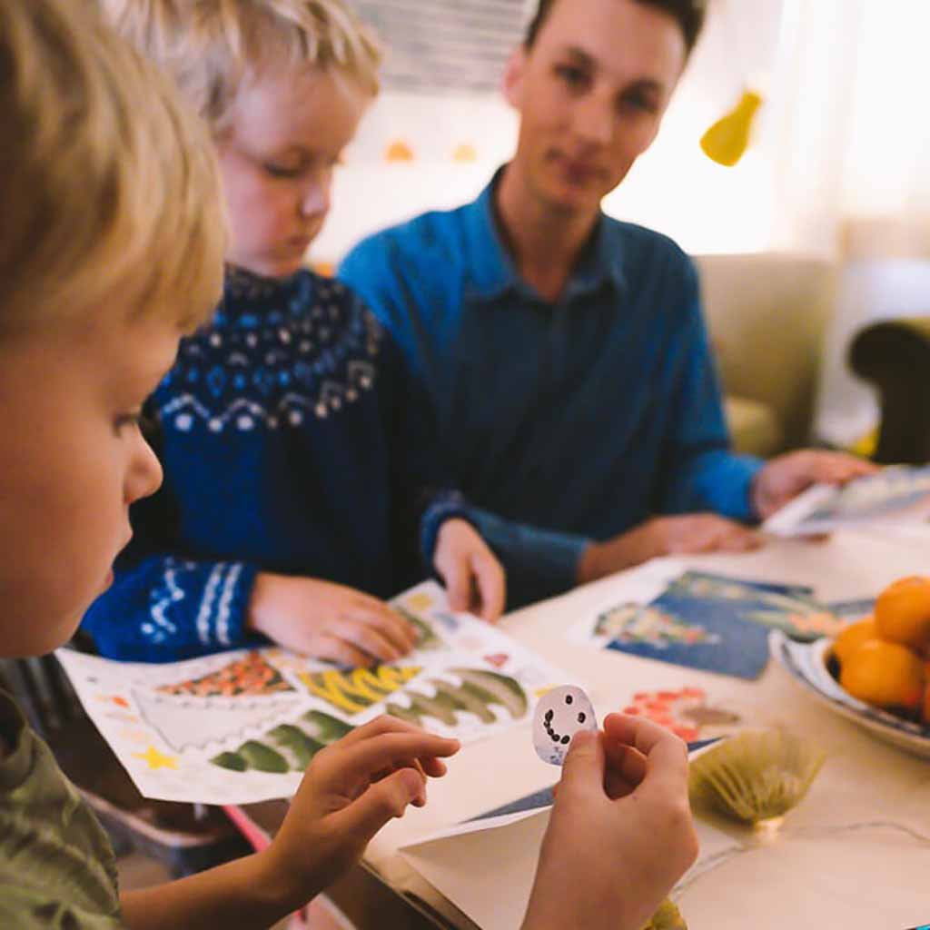 Family sitting around a table with children engaged in making their own christmas cards.