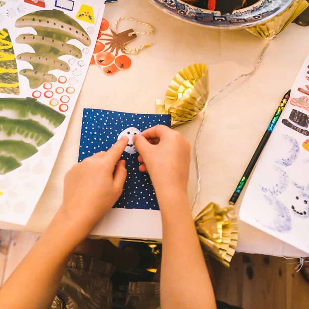 Child's hands holding a snowman craft on a table with art supplies