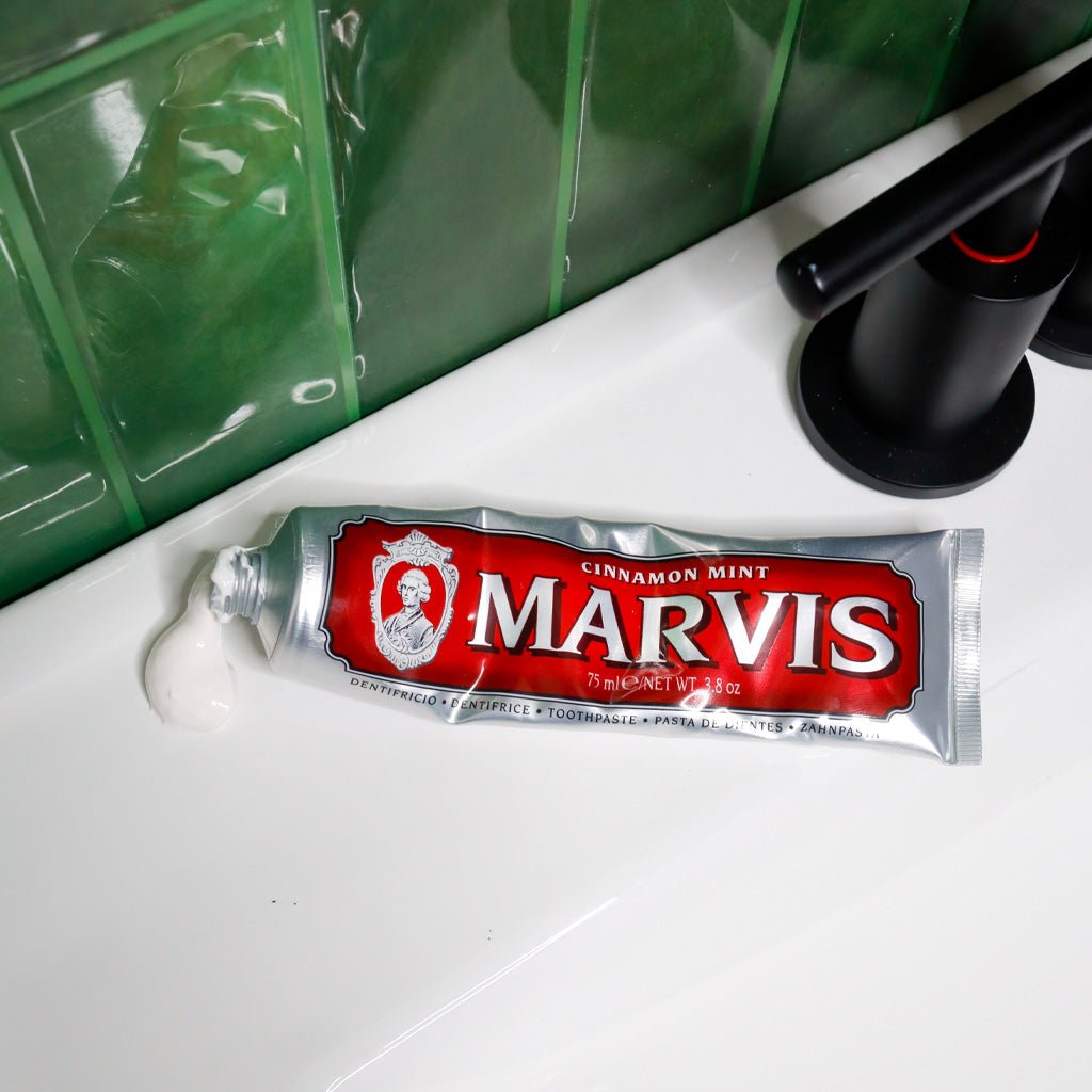 Open Marvis Cinnamon Mint toothpaste tube with toothpaste on bathroom sink.