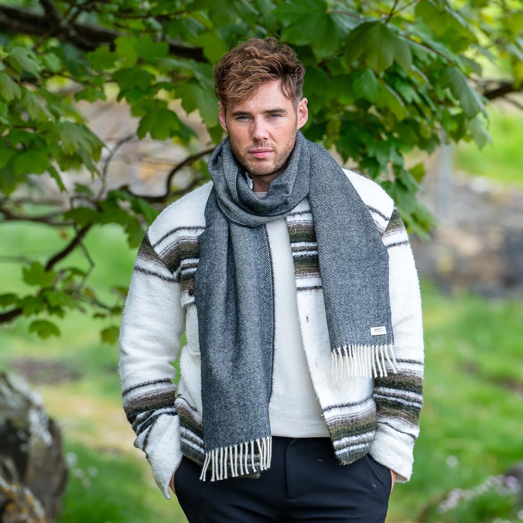 A man wearing a black herringbone wool scarf in front of a natural background.