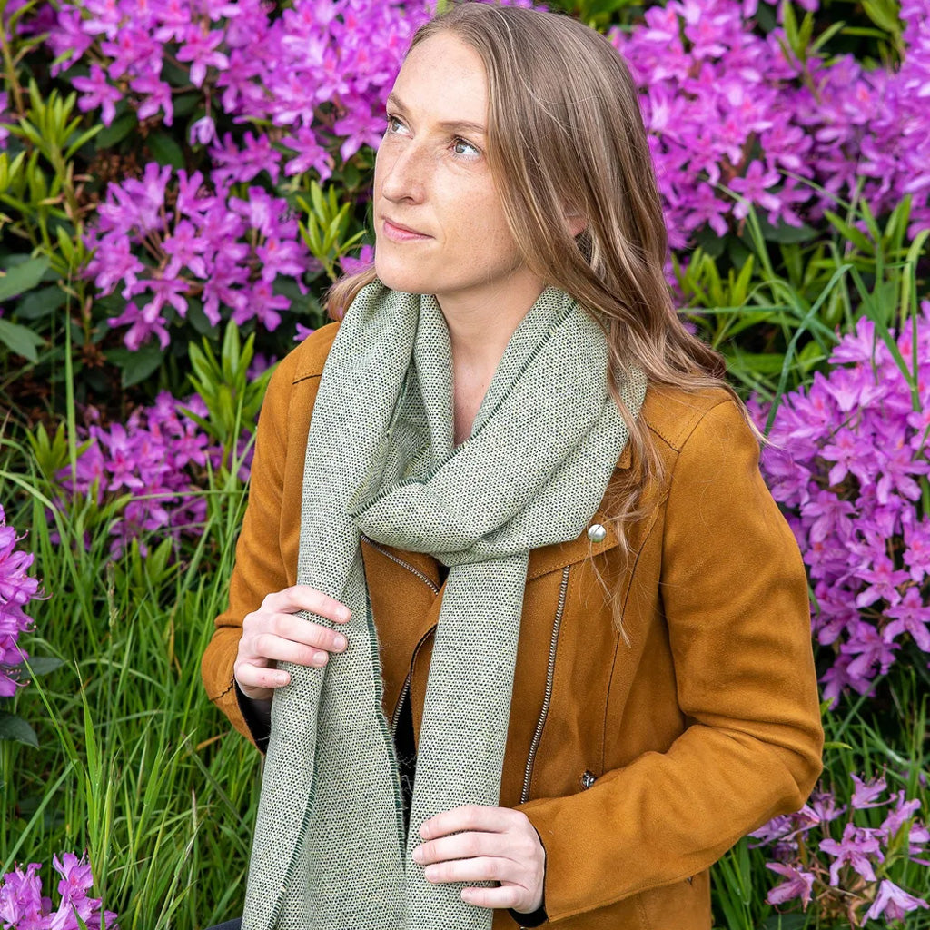 Woman wearing a sage green scarf in front of floral background.