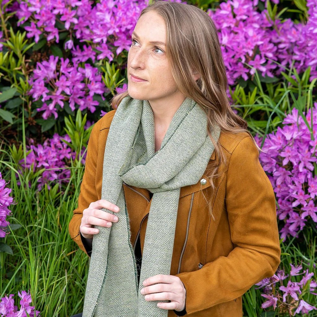 Woman wearing a sage green scarf in front of floral background.