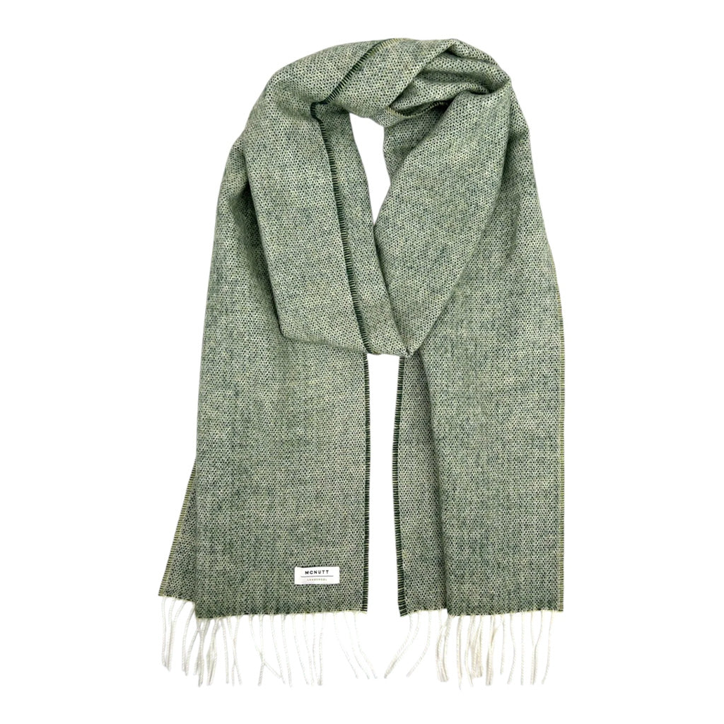 A sage green merino wool scarf laid in a loop on a white background.