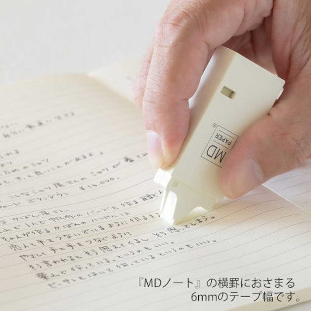 Hand using MD paper correction tape dispenser on page with Japanese text