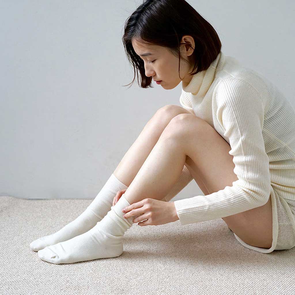 Woman sitting on the floor wearing white socks and a cream-colored outfit.