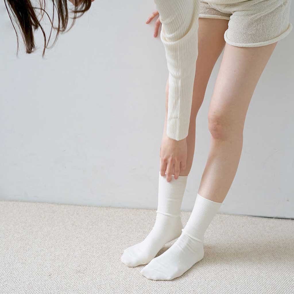 Person wearing white knee-high socks and light-colored pants on a plain background