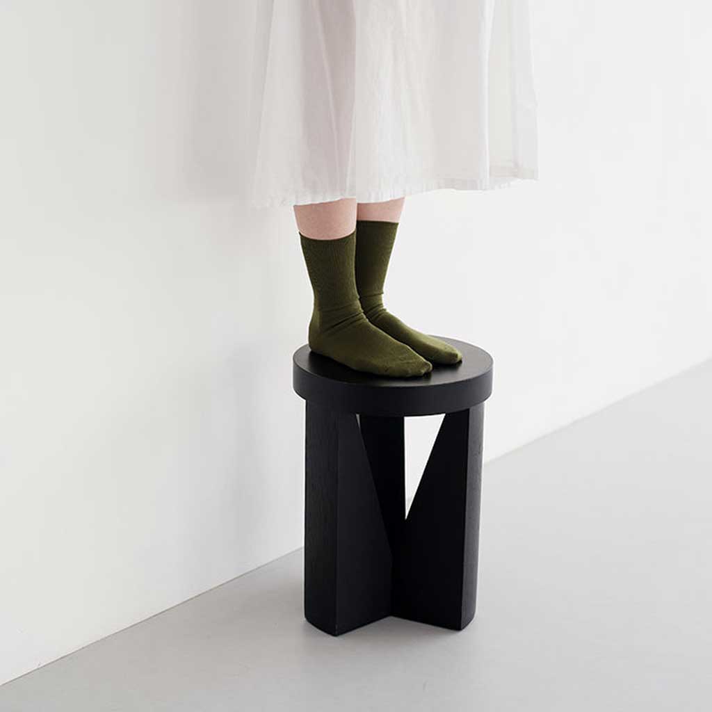 Person wearing green socks standing on a black stool against a white background