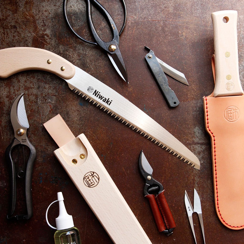 Collection of gardening tools including a saw, shears, and pruners on a rustic surface with 'Niwaki' branding.