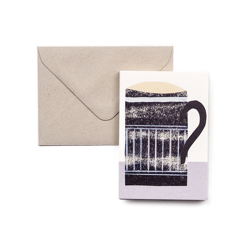 Greeting card featuring an illustrated black-and-cream striped mug, shown in front of a kraft paper envelope.