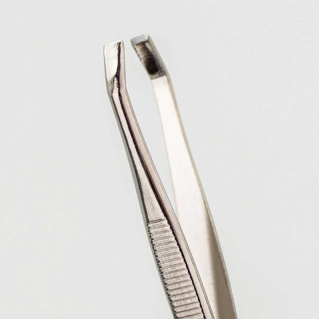 Pair of silver tweezers with clawed tips on a light gray background