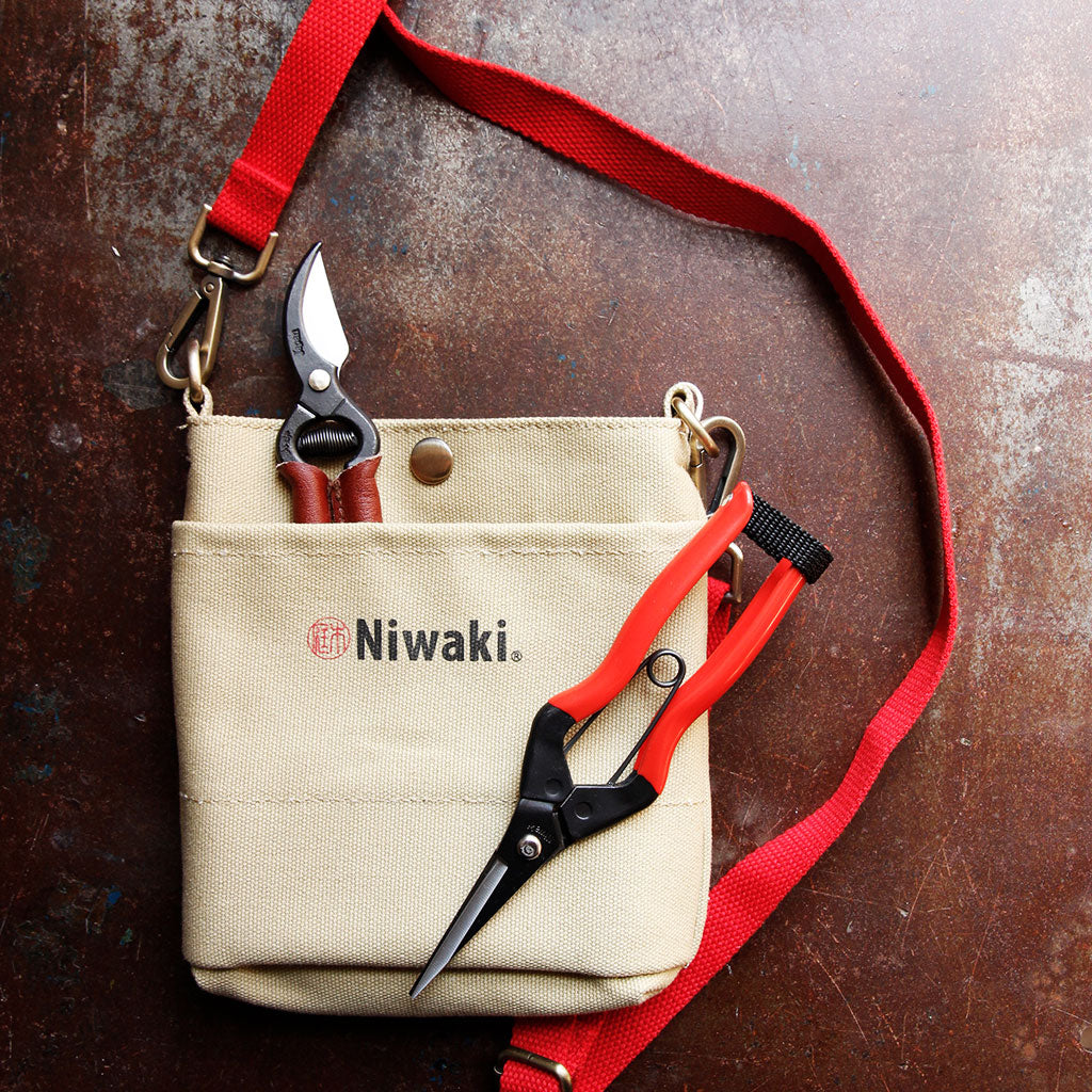 Niwaki snips and shears inside canvas garden pouch with red strap on dark background