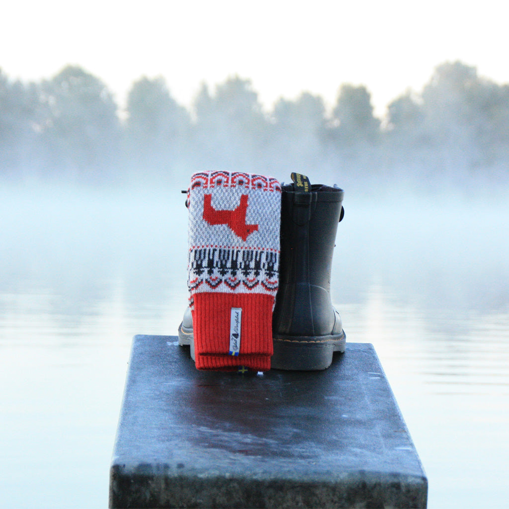 A red and white wool socks tucked into rubber boots on dock.