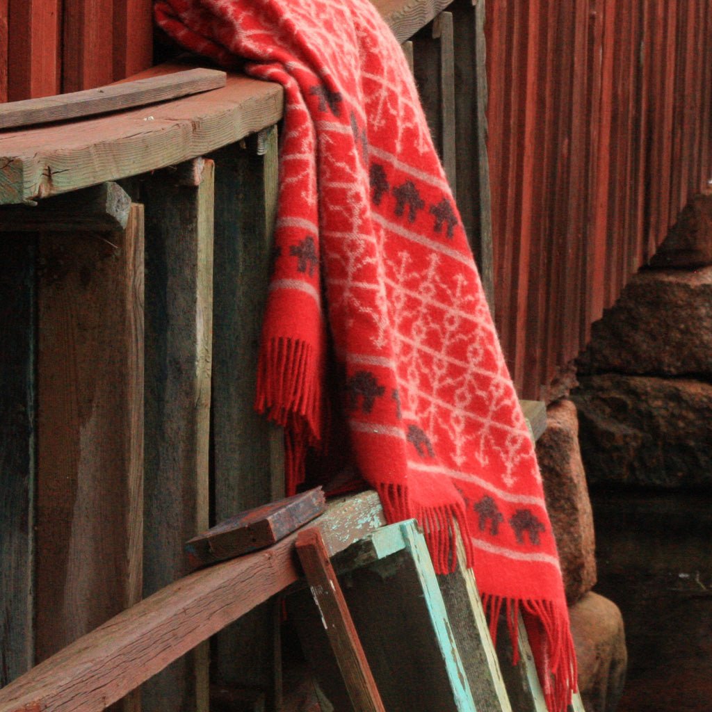 Red wool blanket hanging on wooden planks.