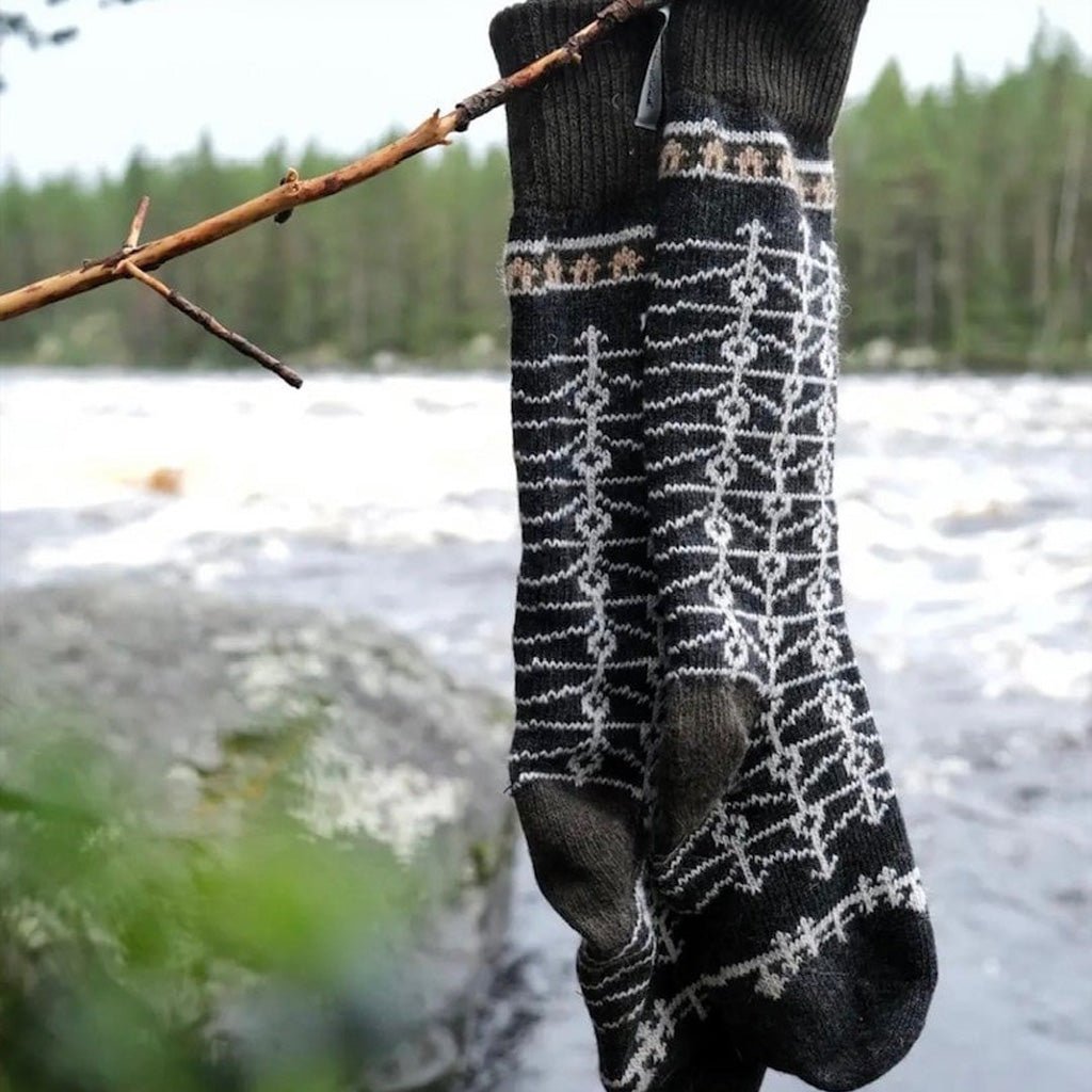 Pair of patterned wool socks hanging on tree branch in front of water setting.