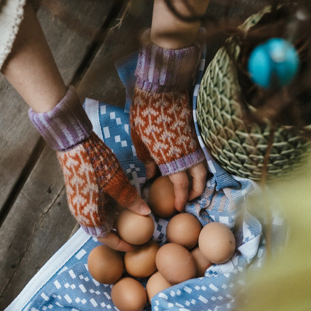 Hands wearing patterned wool wristwarmers and placing eggs onto cloth.