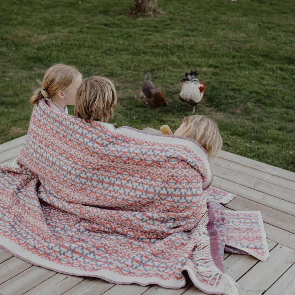 Group of kids wrapped in Lycksele wool blanket outside.