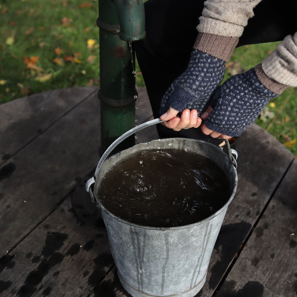 Hands wearing wool wrist warmers, carrying metal bucket of water.