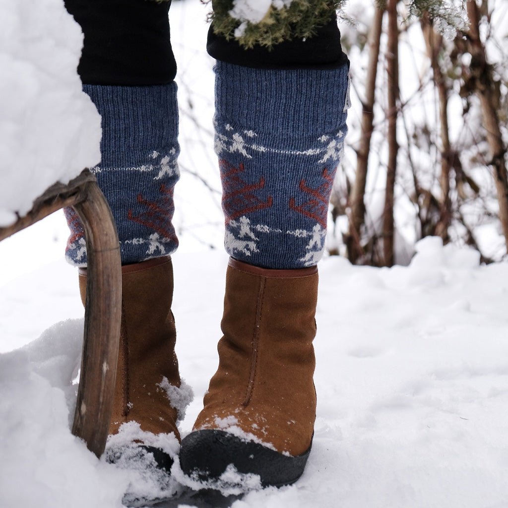 Model wearing blue wool socks and brown boots in snowy setting.