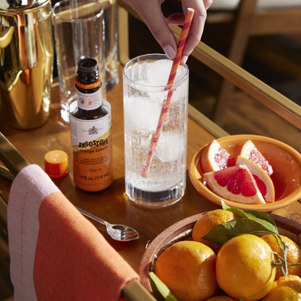 Bottle of Angostura orange bitters next to fizzy drink on bar cart