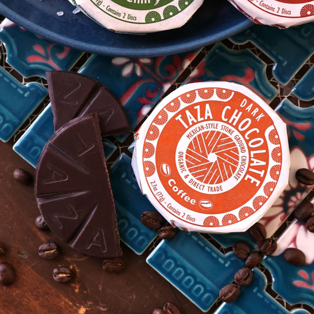 Taza Chocolate packaging with dark chocolate pieces and coffee beans on a decorative surface