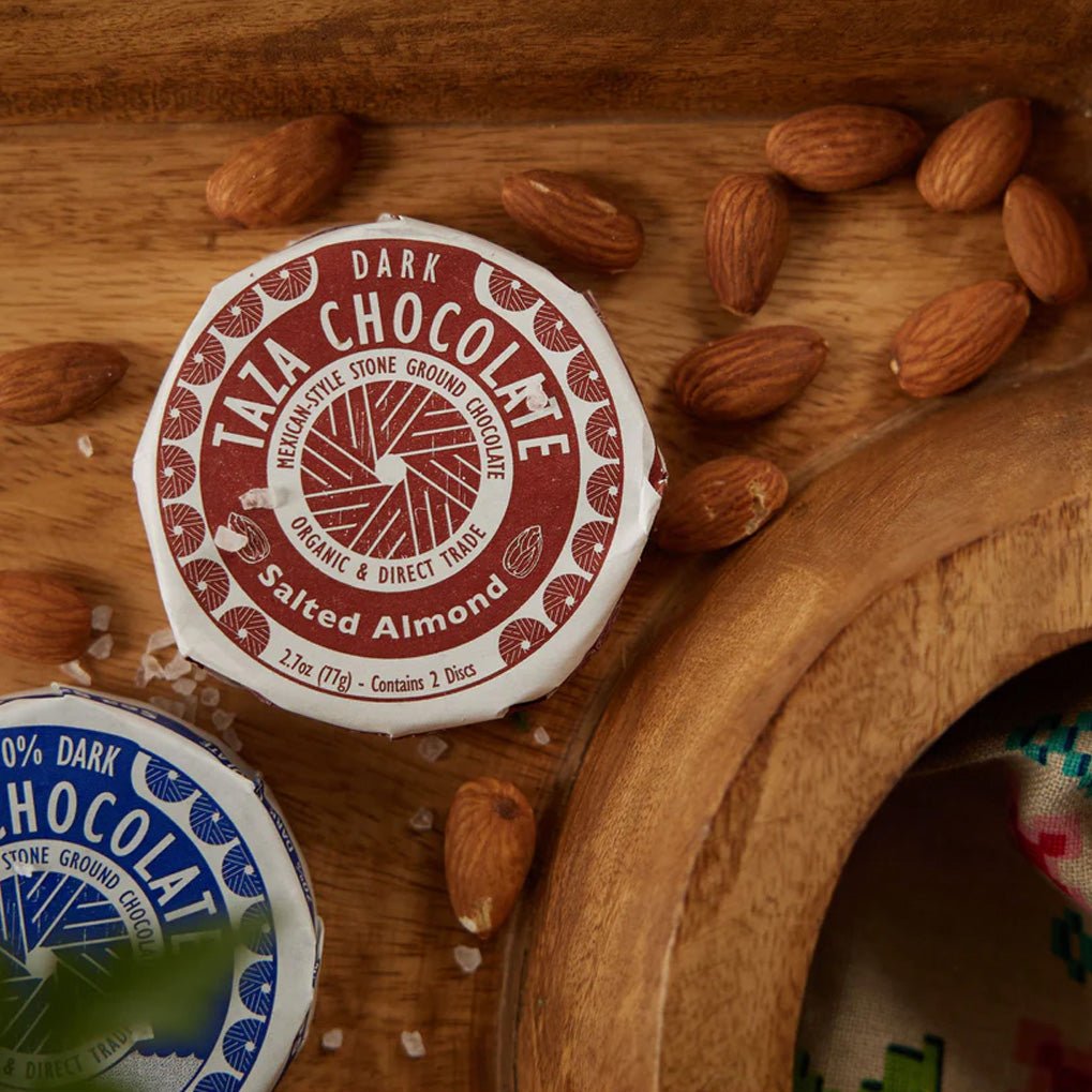 Taza Chocolate dark chocolate salted almond packaging on a wooden surface with almonds around.