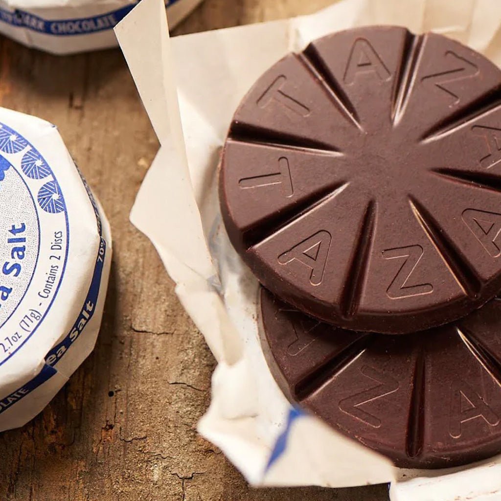 Round chocolate tablets with 'TAZA' branding on a wooden surface.