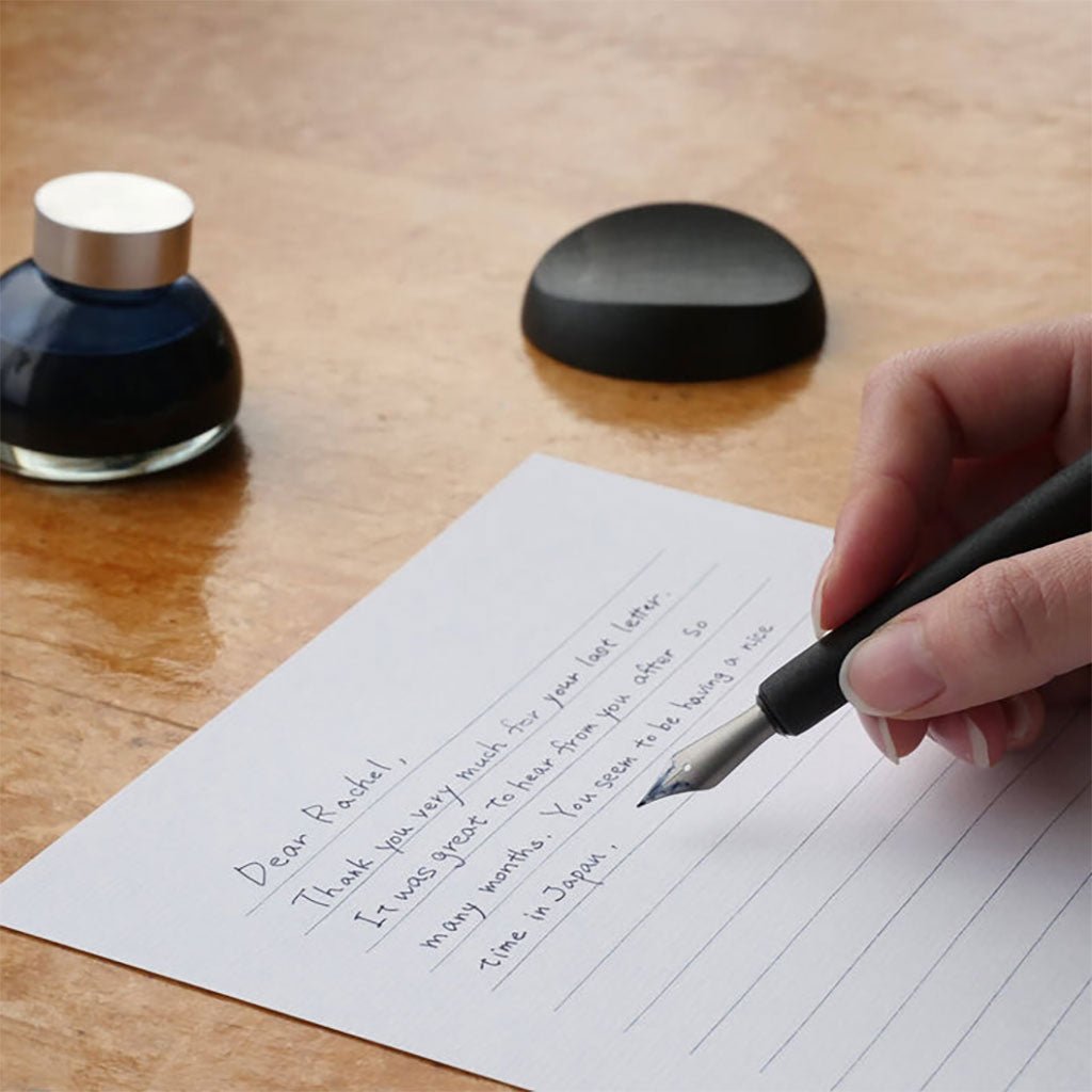 Hand writing on a piece of paper with a fountain pen and ink bottle on a wooden surface