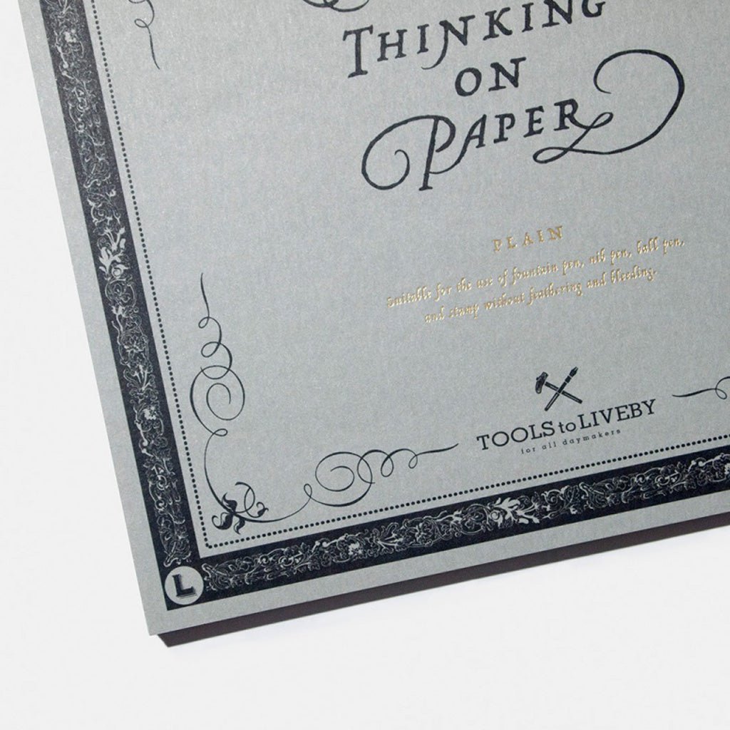 A gray square plain practice paper pad with "Writing Is Thinking On Paper" design against white background