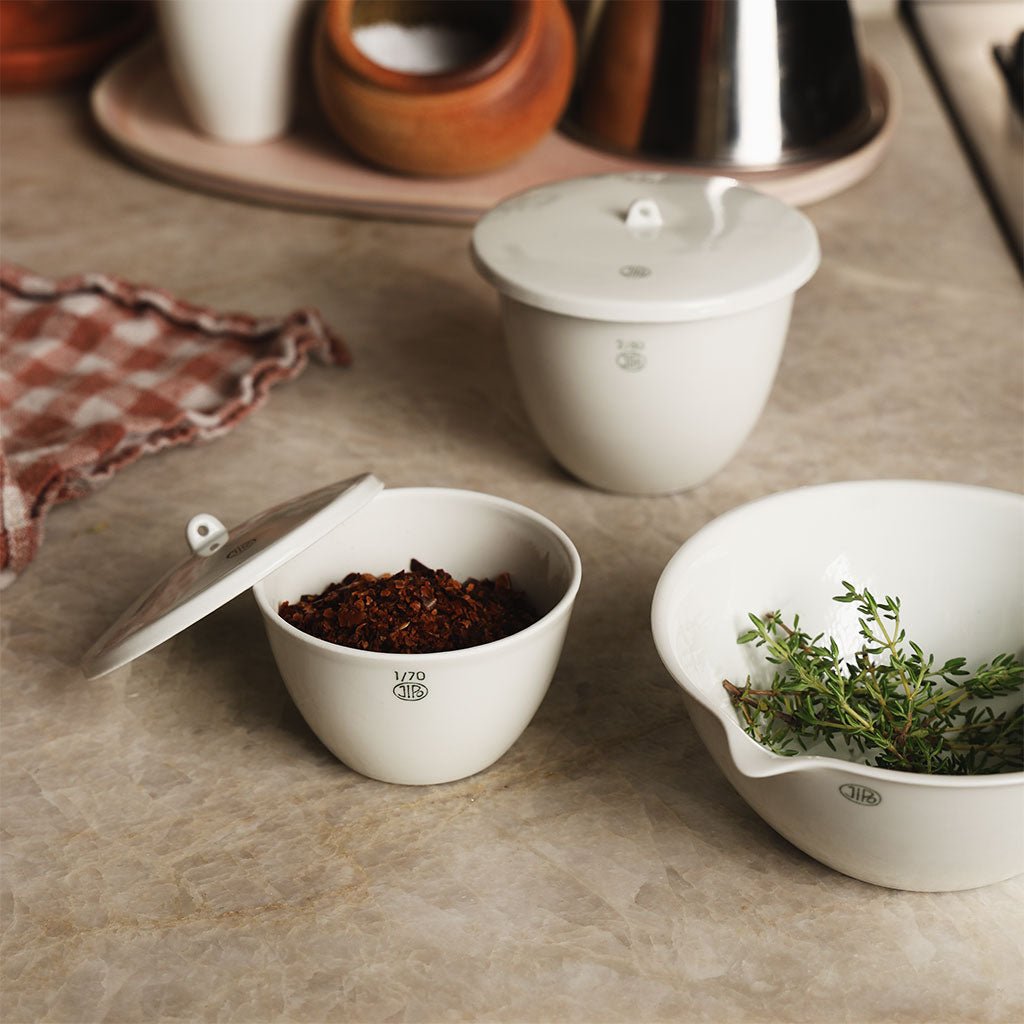 White porcelain jar and bowl filled with spices and herbs on kitchen counter.