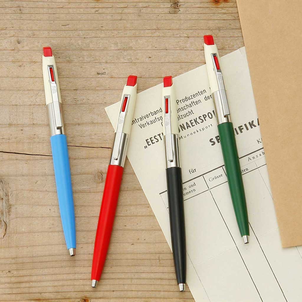 Four colorful pens on a wooden surface with a newspaper underneath