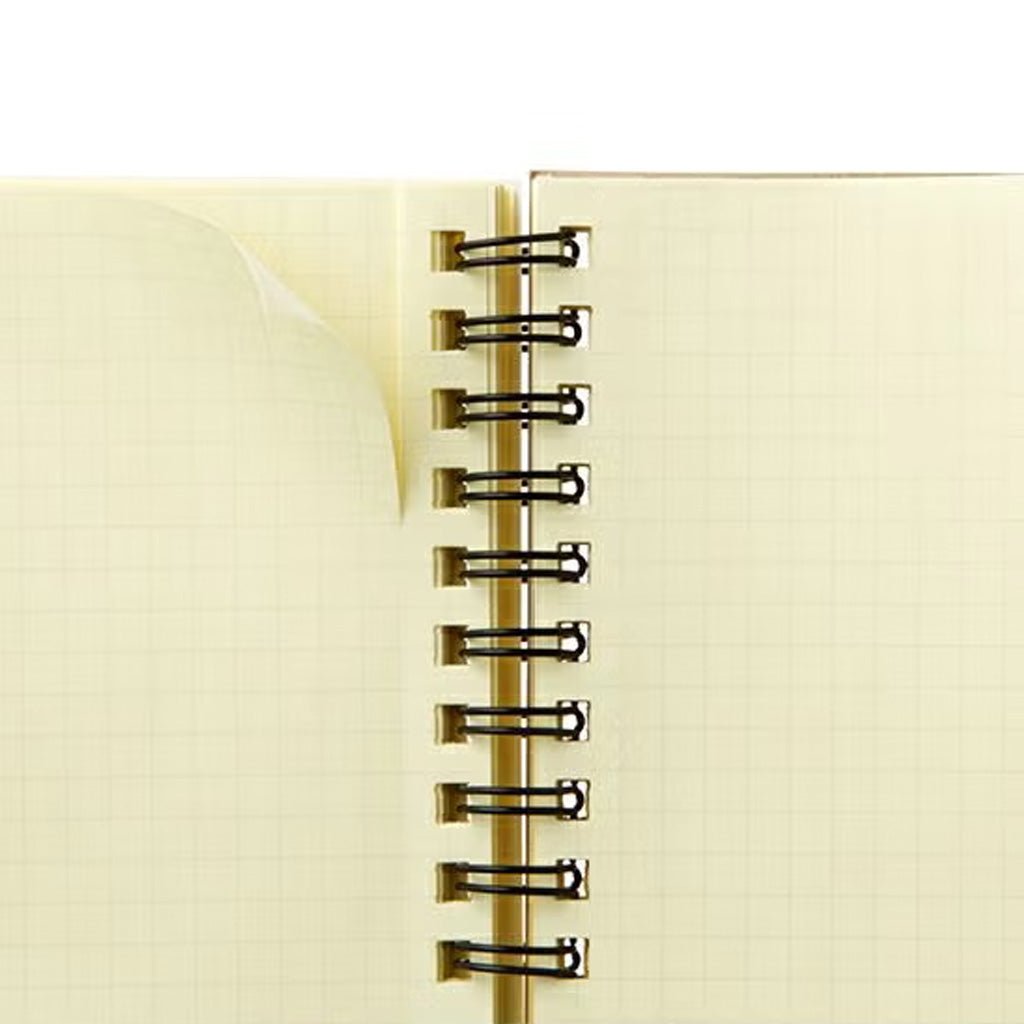 A close-up of an open spiral-bound notebook with cream-colored graph paper pages and black metal wire binding.