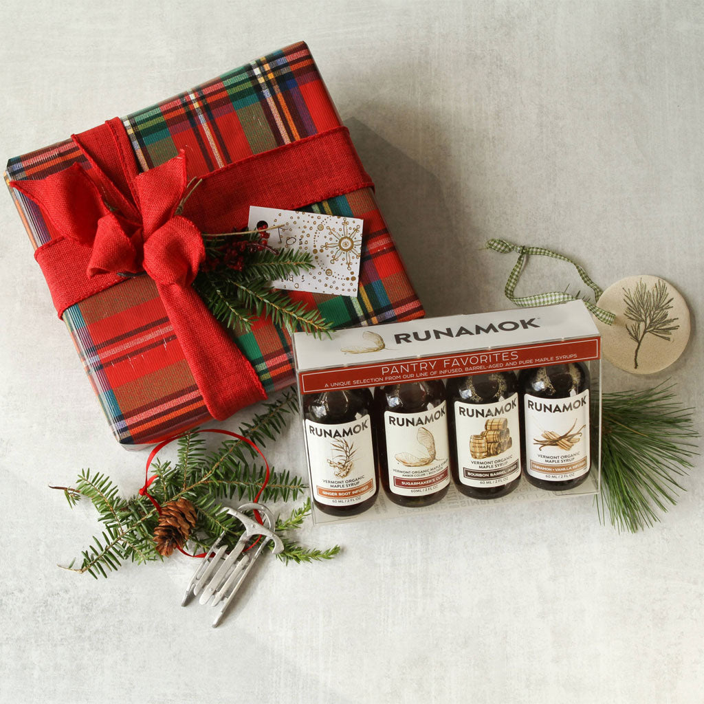 Set of Runamok maple syrup bottles next to festive wrapped present and sprigs of holly.
