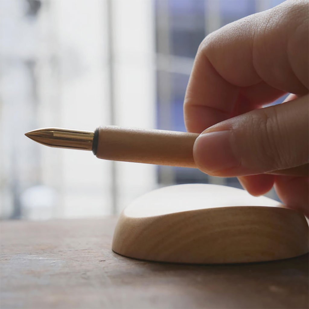 Hand holding a pen over a wooden pen rest with a blurred background