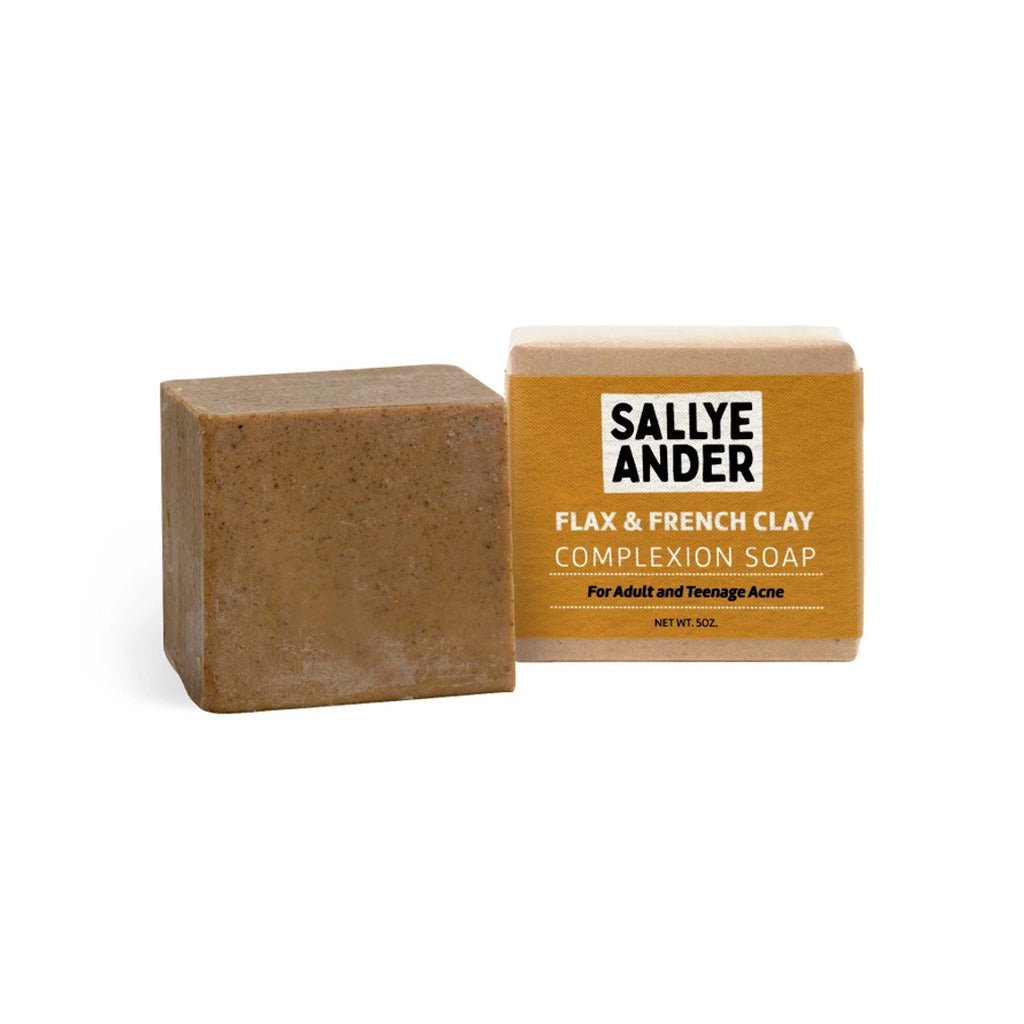 A bar of brown speckled flax and French clay facial complexion soap next to bar in packagin with yellow label and SallyeAnder branding on white background