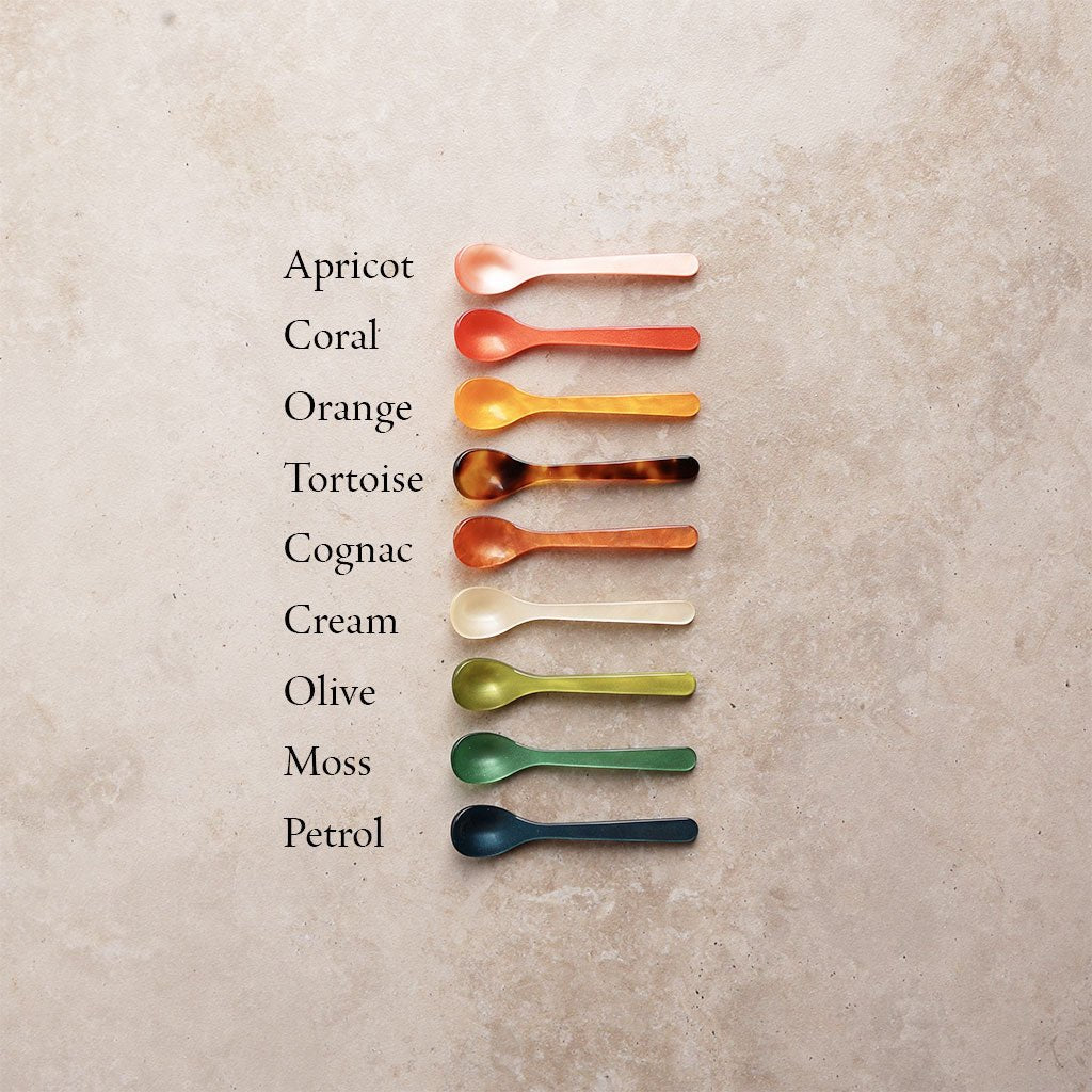 Set of colorful spoons arranged in a row on a textured surface with color names listed.