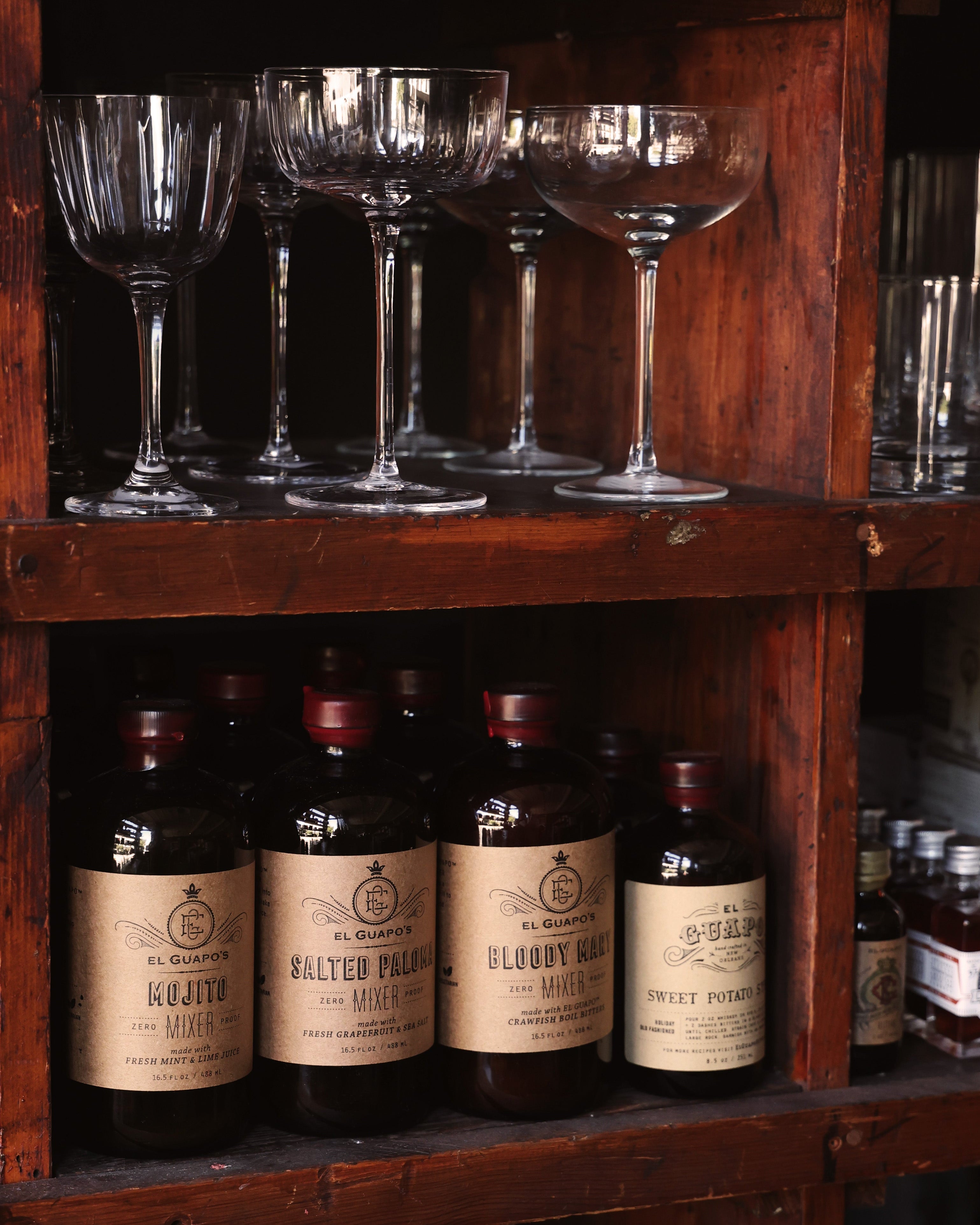 Glassware and bottled cocktail mixers on wooden shelving.